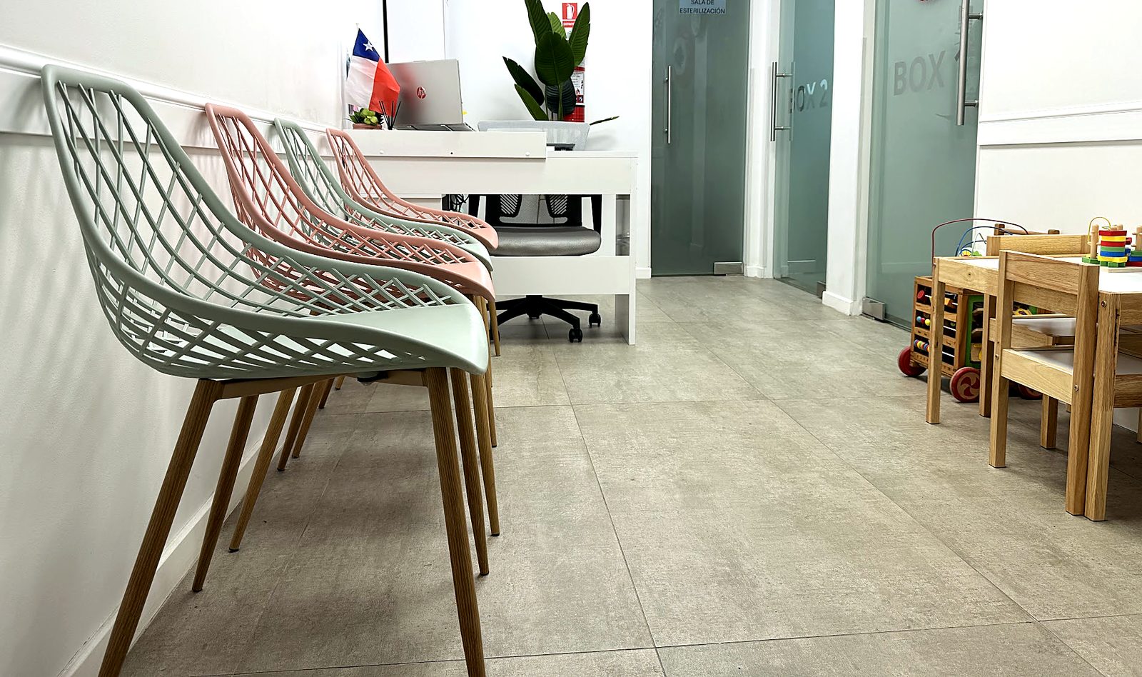 Sala de espera de Magna Clínica con sillas verde agua y rosadas, recepción y rincón infantil